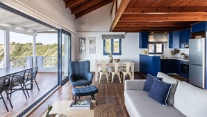 Amplia sala de estar con mesa de comedor, sofá y zona de cocina con armarios azules.