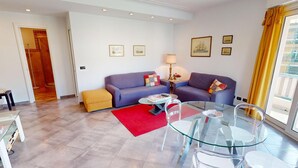 A modern living room with a sofa set, a glass dining table with chairs, a red rug, and a small side table with a lamp. - Cozy 3P with air conditioning and balcony, near beaches (Menton)