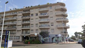 A multi-story residential building with balconies, a ground-level entrance, and a visible sign for a business named "Naturel Coiffure." - Cozy 3P with air conditioning and balcony, near beaches (Menton)