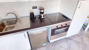A compact kitchen with a stainless steel sink, a coffee maker, a stove, and a dishwasher. - Cozy 3P with air conditioning and balcony, near beaches (Menton)