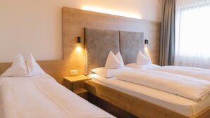 Habitación de hotel con dos camas individuales, cabecero de madera, lámparas de noche y una ventana con cortinas.