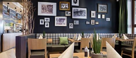 A restaurant with a black wall adorned with framed photographs, wooden furniture, and a checkered bench area.