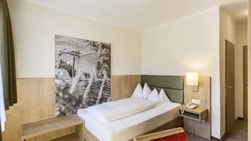 Quarto de hotel com cama, mesa de cabeceira com abajur, telefone e um quadro preto e branco grande na parede.