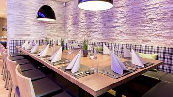 A restaurant with a long wooden table set for a meal, surrounded by black cushioned chairs.