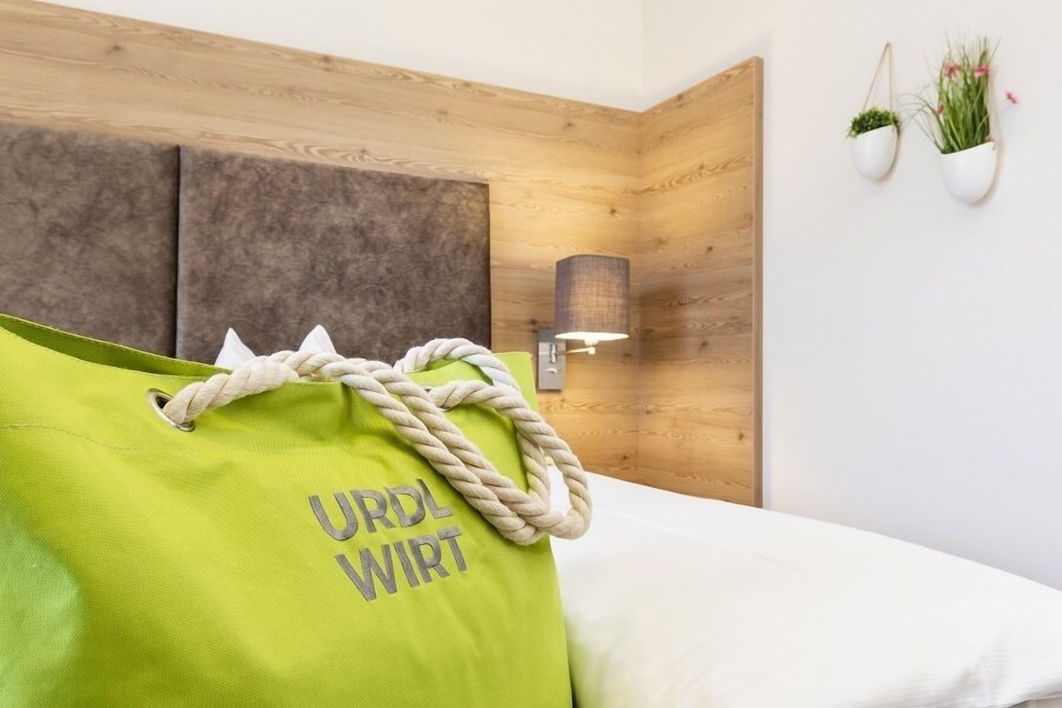 En säng med en grön väska märkt med texten ”URDL WIRT” och en vägglampa.