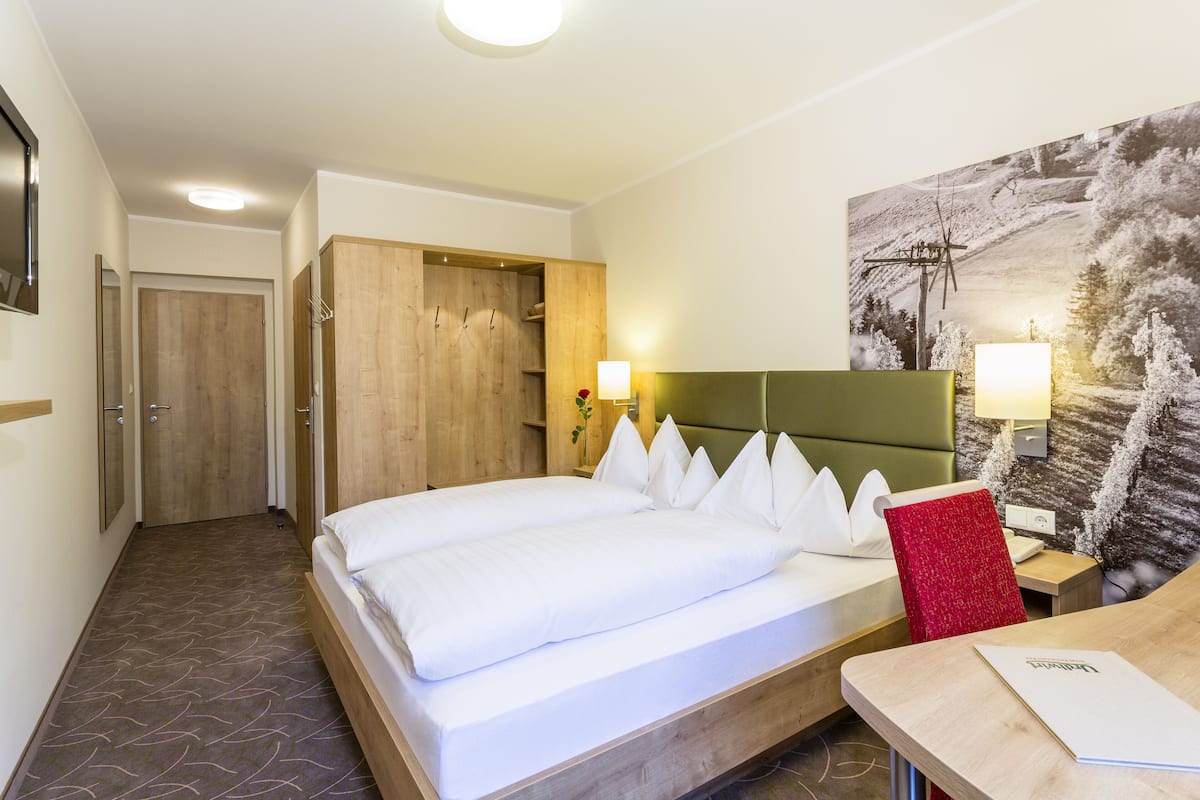 Une chambre d’hôtel avec un lit, un bureau, une chaise, un tableau et une porte.