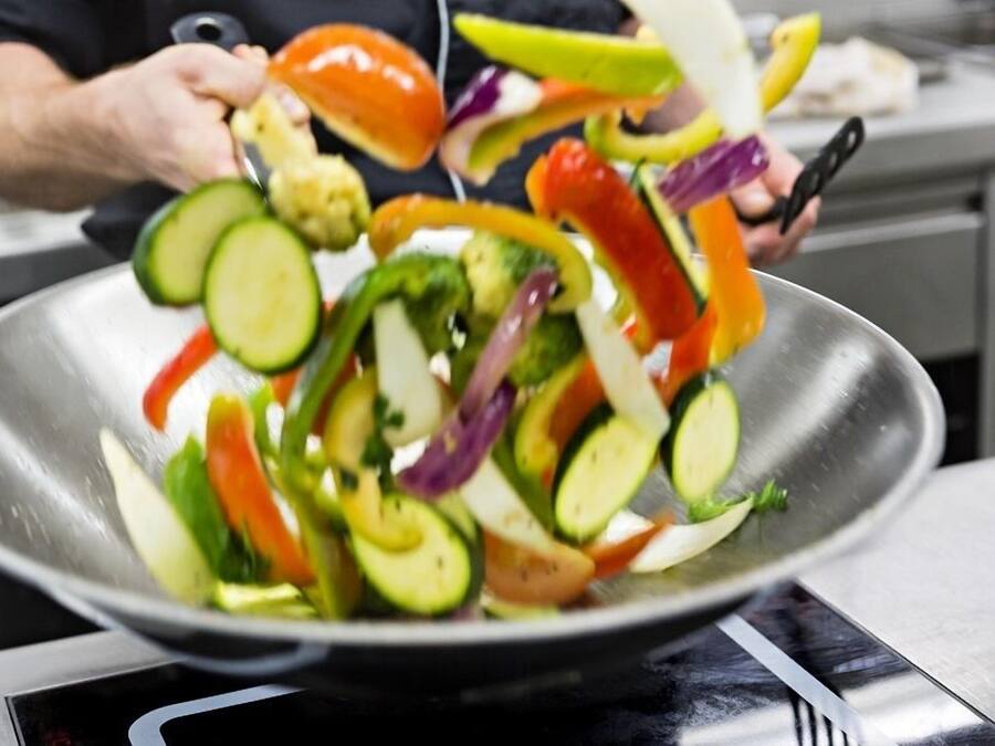 A chef preparing a vegetable stir-fry in a large metal pan.