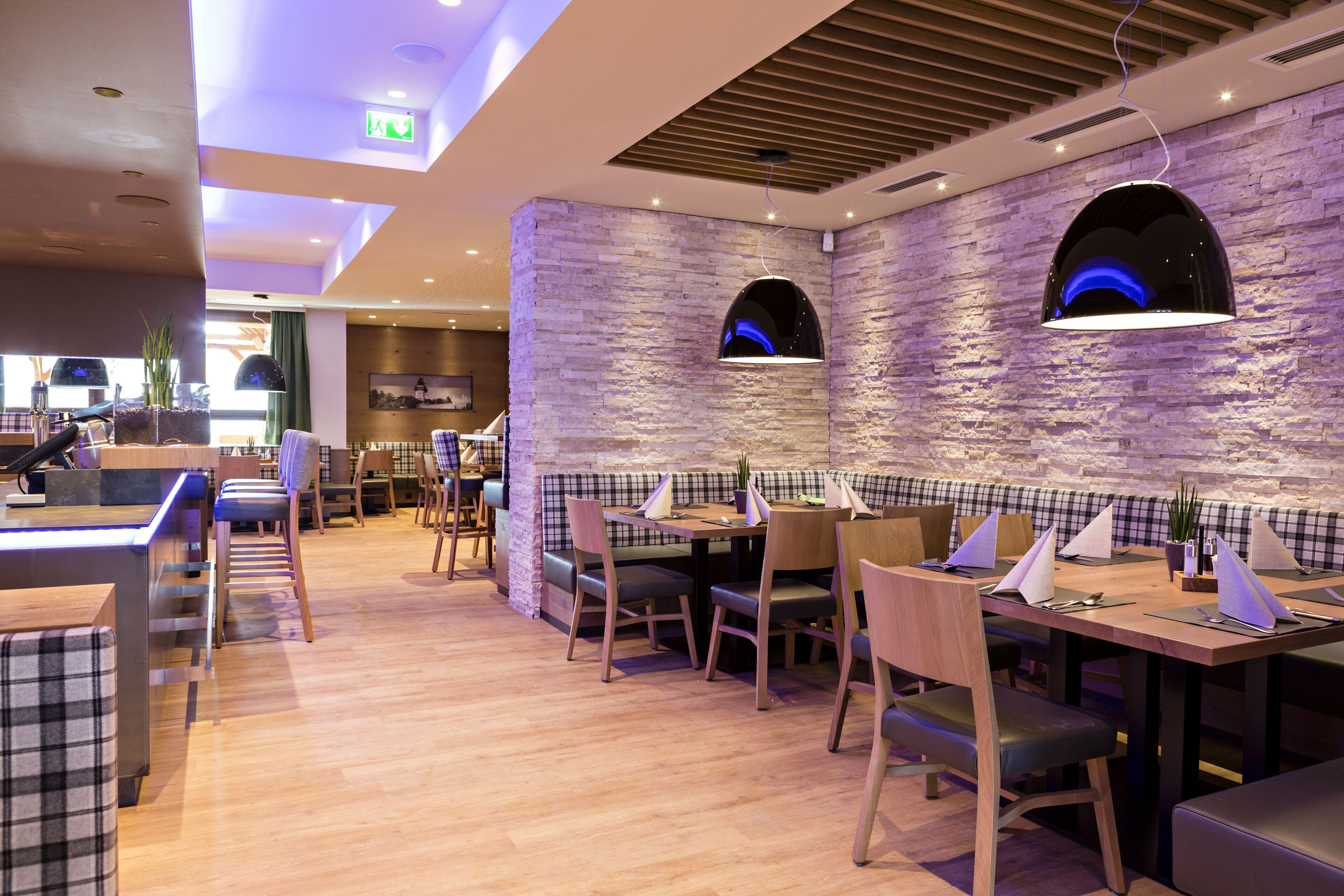 A modern restaurant with wooden flooring, checkered booths, and a stone wall.