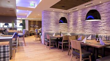 A modern restaurant with wooden flooring, checkered booths, and a stone wall.