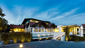 Un hotel moderno con una entrada bien iluminada, un espacio exterior cubierto y un jardín ajardinado.