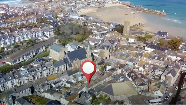 Une vue aérienne d’une ville côtière, avec une grande épingle rouge bien visible sur la carte.