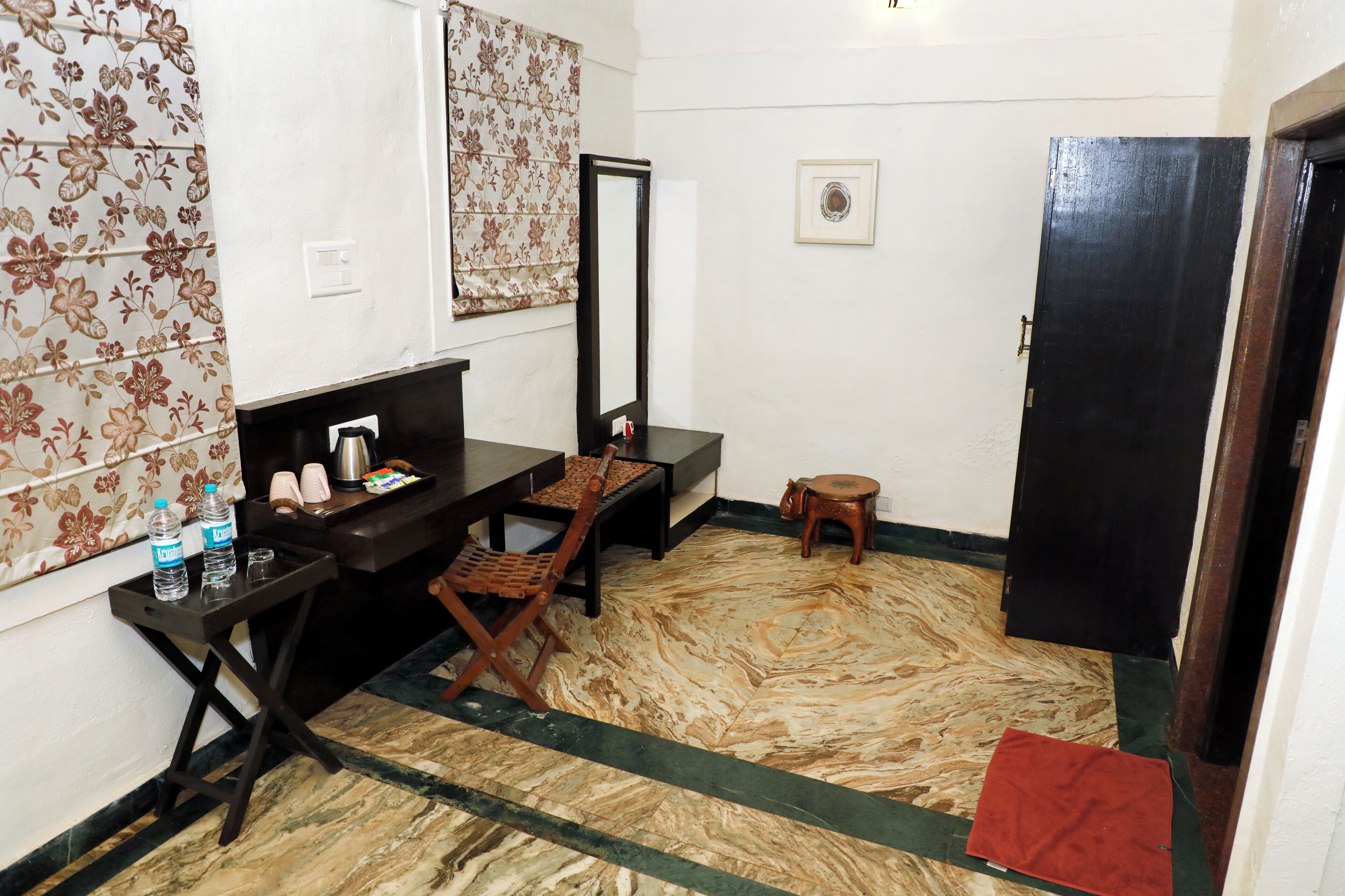 A small room with a desk, chair, and a mirror. There is a small stool and a red mat on the floor.