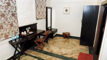 A small room with a desk, chair, and a mirror. There is a small stool and a red mat on the floor.