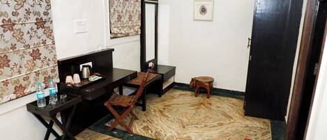 A small room with a desk, chair, and a mirror. There is a small stool and a red mat on the floor.
