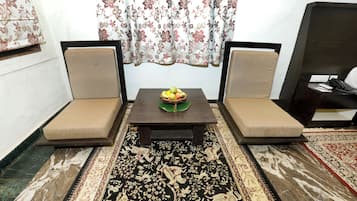 Een kamer met twee fauteuils, een tafeltje met fruit en een kamerbreed tapijt met patroon.
