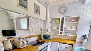 A compact kitchen with a microwave, toaster, and small refrigerator. There is a sink with a faucet and a clock on the wall. - St Ives town cottage - family & pets - sleeps 4, Holiday Cottages St Ives (St Ives)