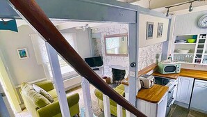 A staircase leading to a living area with a fireplace, a kitchen with a microwave, and a dining table with chairs. - St Ives town cottage - family & pets - sleeps 4, Holiday Cottages St Ives (St Ives)
