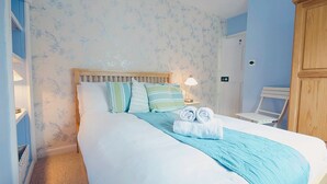 A neatly made bed with a blue bedspread, pillows, and a rolled towel. - St Ives town cottage - family & pets - sleeps 4, Holiday Cottages St Ives (St Ives)