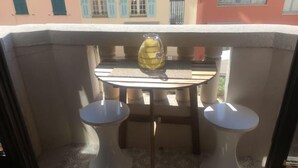 Un pequeño balcón con una mesa, dos taburetes, un jarrón amarillo y un suelo estampado.