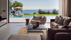 A modern living room with a large glass door leading to a pool and ocean view. - Omnia Villa (Zakynthos)