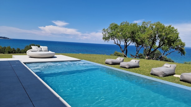 A modern outdoor pool area with a view of the sea, equipped with lounge chairs and a sofa. - Omnia Villa (Zakynthos)