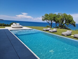 A modern outdoor pool area with a view of the sea, equipped with lounge chairs and a sofa. - Omnia Villa (Zakynthos)