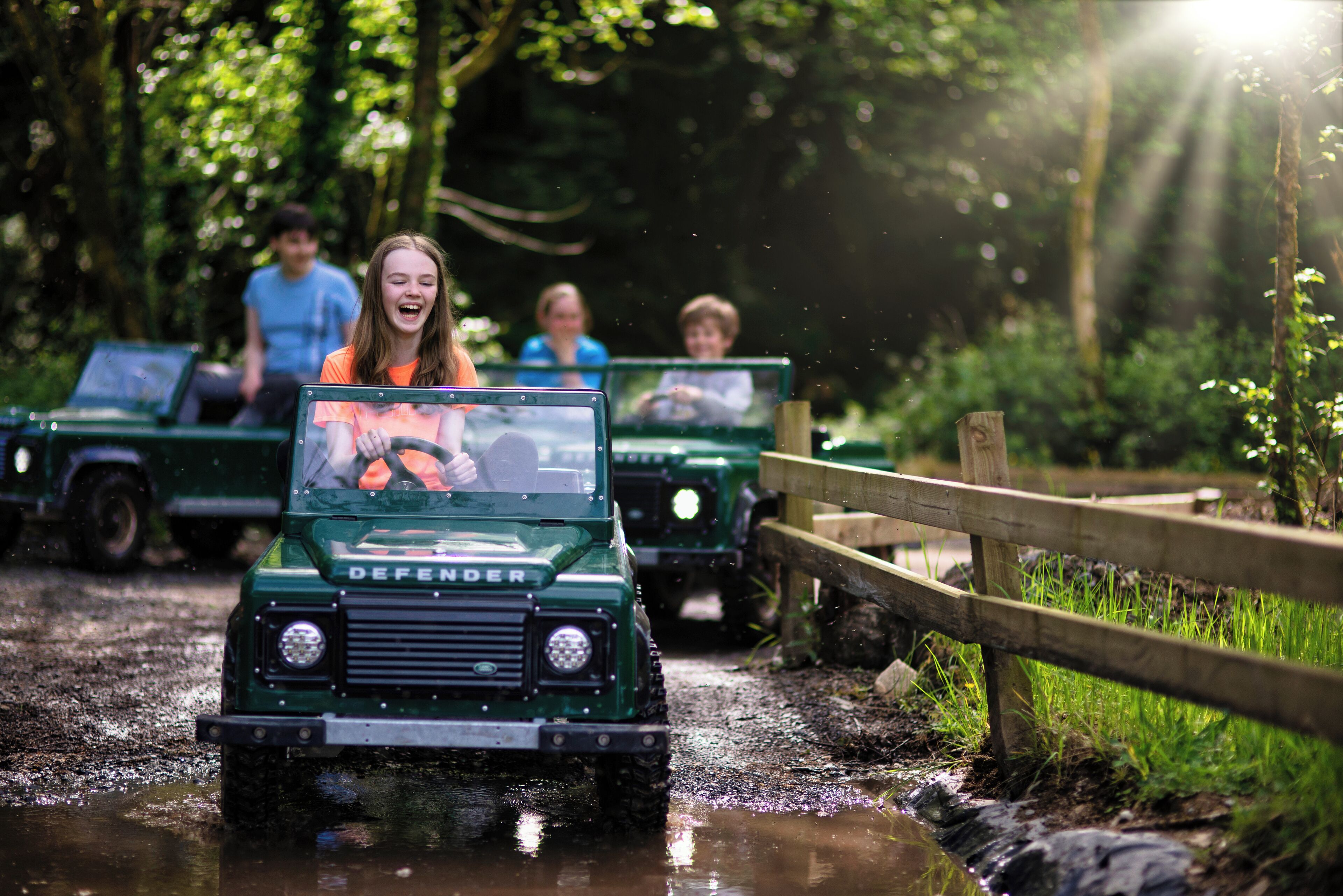 A green Defender vehicle driving through a muddy path with passengers.