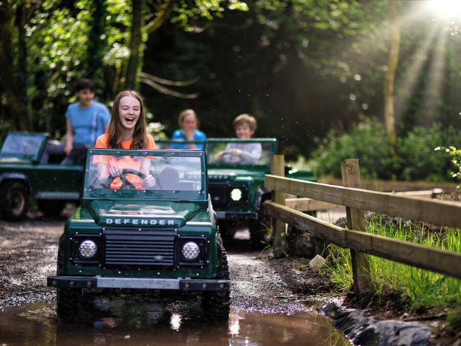 A green Defender vehicle driving through a muddy path with passengers.