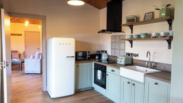 A kitchen with light blue cabinets, a white refrigerator, a wooden countertop, and a black hanging light fixture.