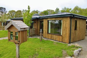 Una cabaña de madera con un ventanal grande y una estructura pequeña adosada con techo inclinado.