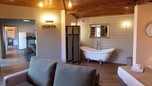 A spacious room with a wooden ceiling, a large bathtub, a sofa, and a dining area visible in the background.