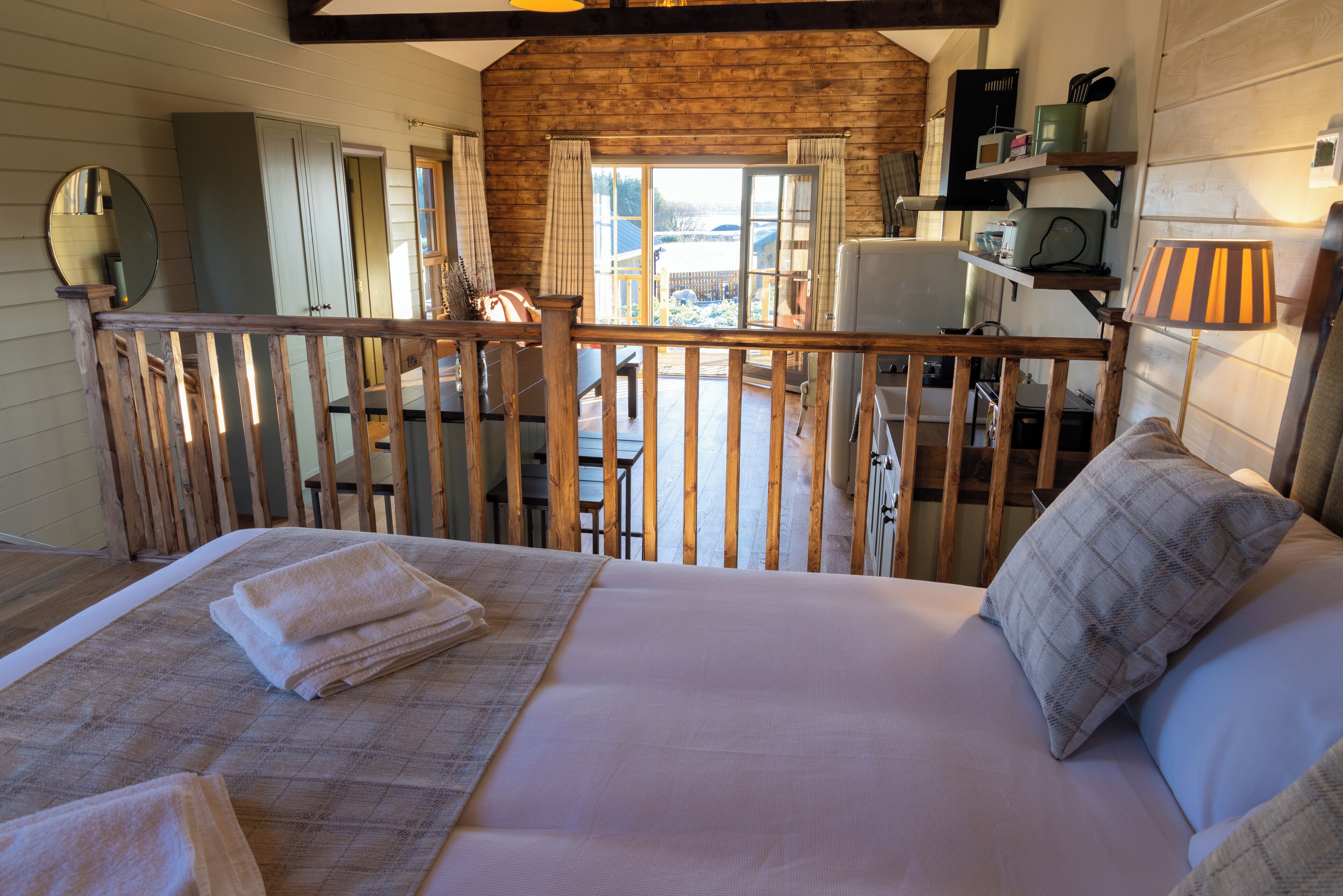 Ein gemütliches Schlafzimmer mit einem großen Bett, einer Holzbalkonage und Blick ins Freie.