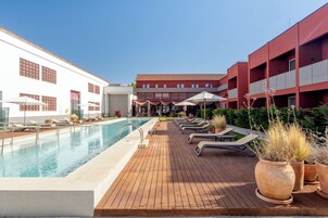 A pool area with lounge chairs and umbrellas, surrounded by buildings with red and white facades.