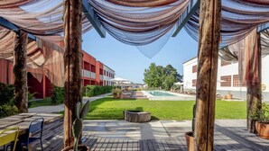 Un espacio patio al aire libre con suelo de madera, una planta de cactus, un banco de madera y una piscina al fondo.
