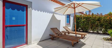 A patio with two wooden lounge chairs and a white umbrella.