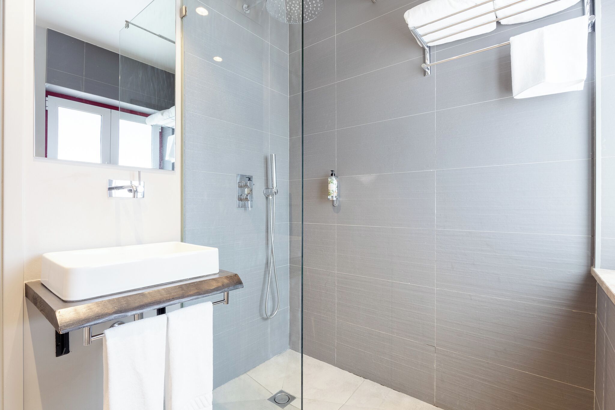 A modern bathroom with a glass-enclosed shower, a white sink, and a large mirror.