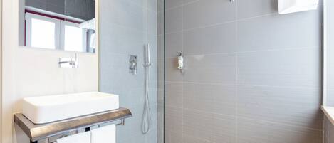 A modern bathroom with a glass-enclosed shower, a white sink, and a large mirror.