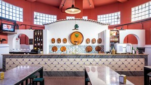 Un restaurante con zona de bar, salpicadero de azulejos y una pantalla de televisión mostrando un programa.