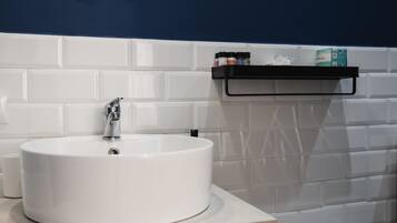 Un lavamanos blanco con un grifo moderno, un jabonera negra y una pared con azulejos blancos.