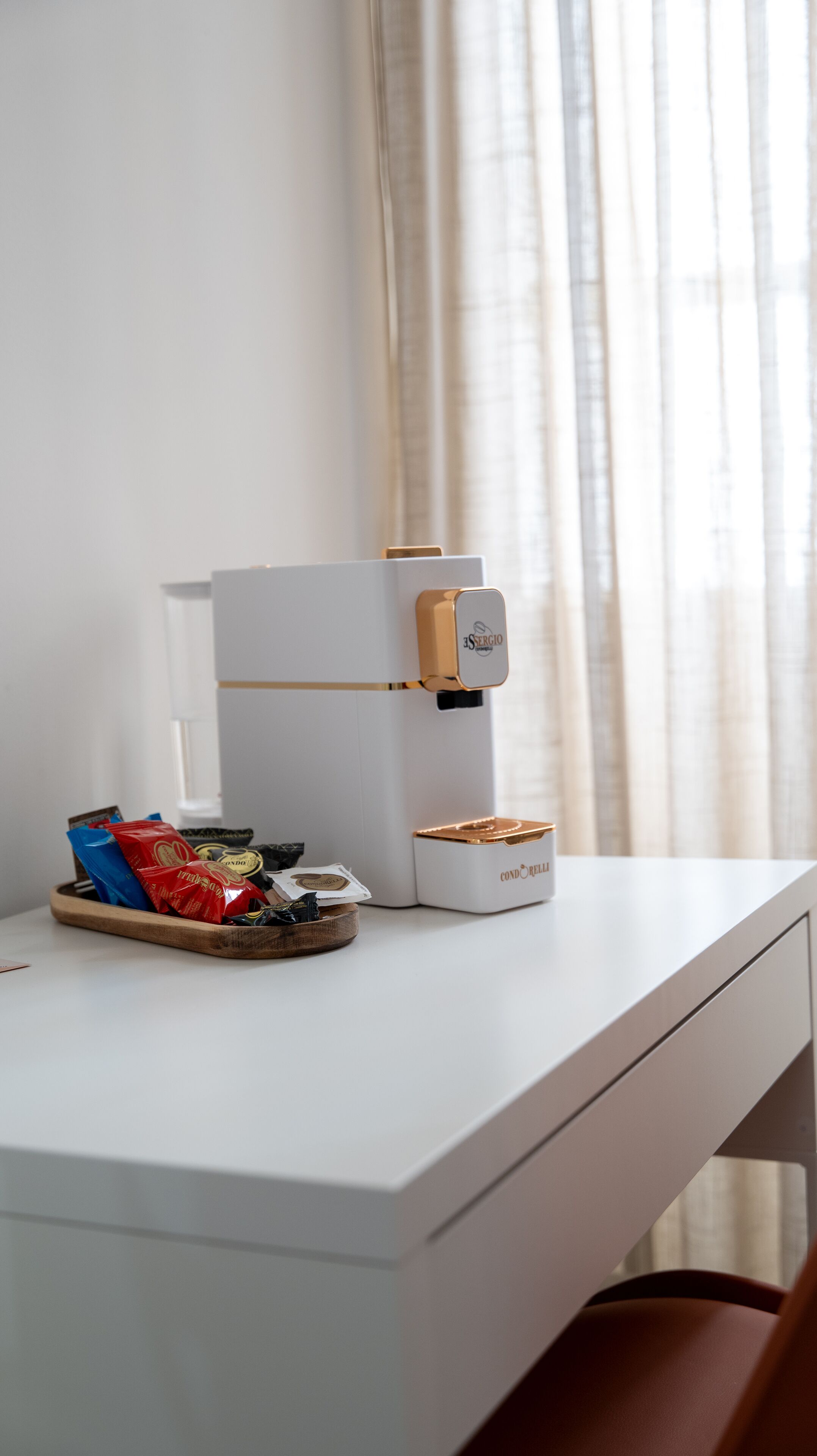 A white desk with a coffee machine, a tray with snacks, and a small container of coffee.