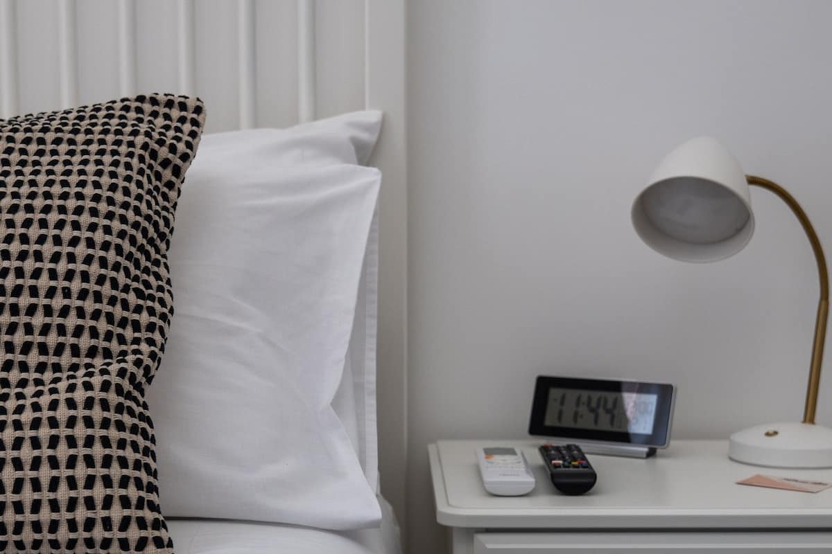 Un lit bien fait, avec des oreillers à motifs et unis, une table de chevet avec une horloge, une lampe et un tiroir.
