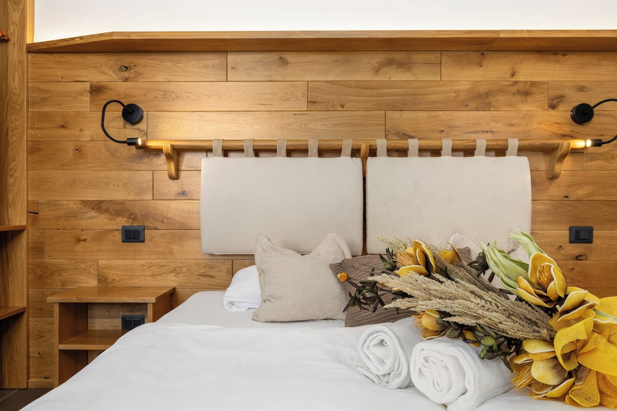 A neatly made bed with white linens, a beige pillow, and a bouquet of yellow flowers.