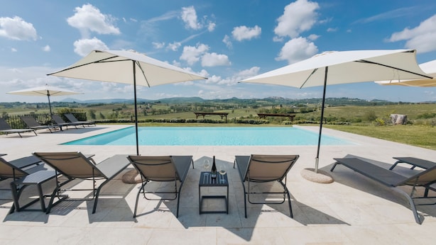 Área à beira da piscina com espreguiçadeiras e guarda-sóis, vista desobstruída da paisagem e uma estrutura de pérgola.