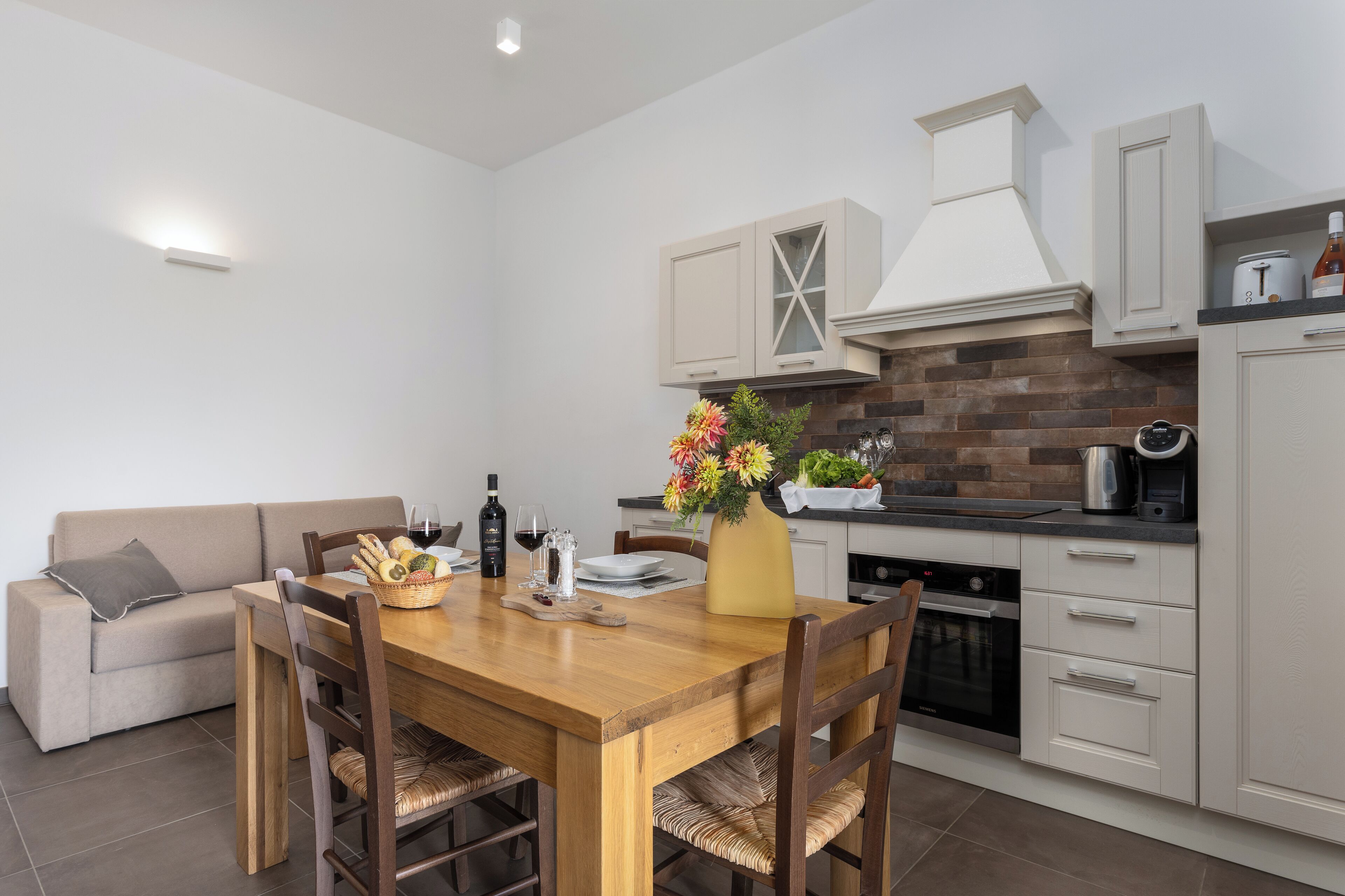 Eine moderne Küche mit Holztisch, weißen Schränken und einer Backstein-Spritzwand.
