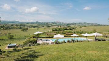 A pool area with umbrellas, a hot tub, and a view of a vineyard and distant hills.