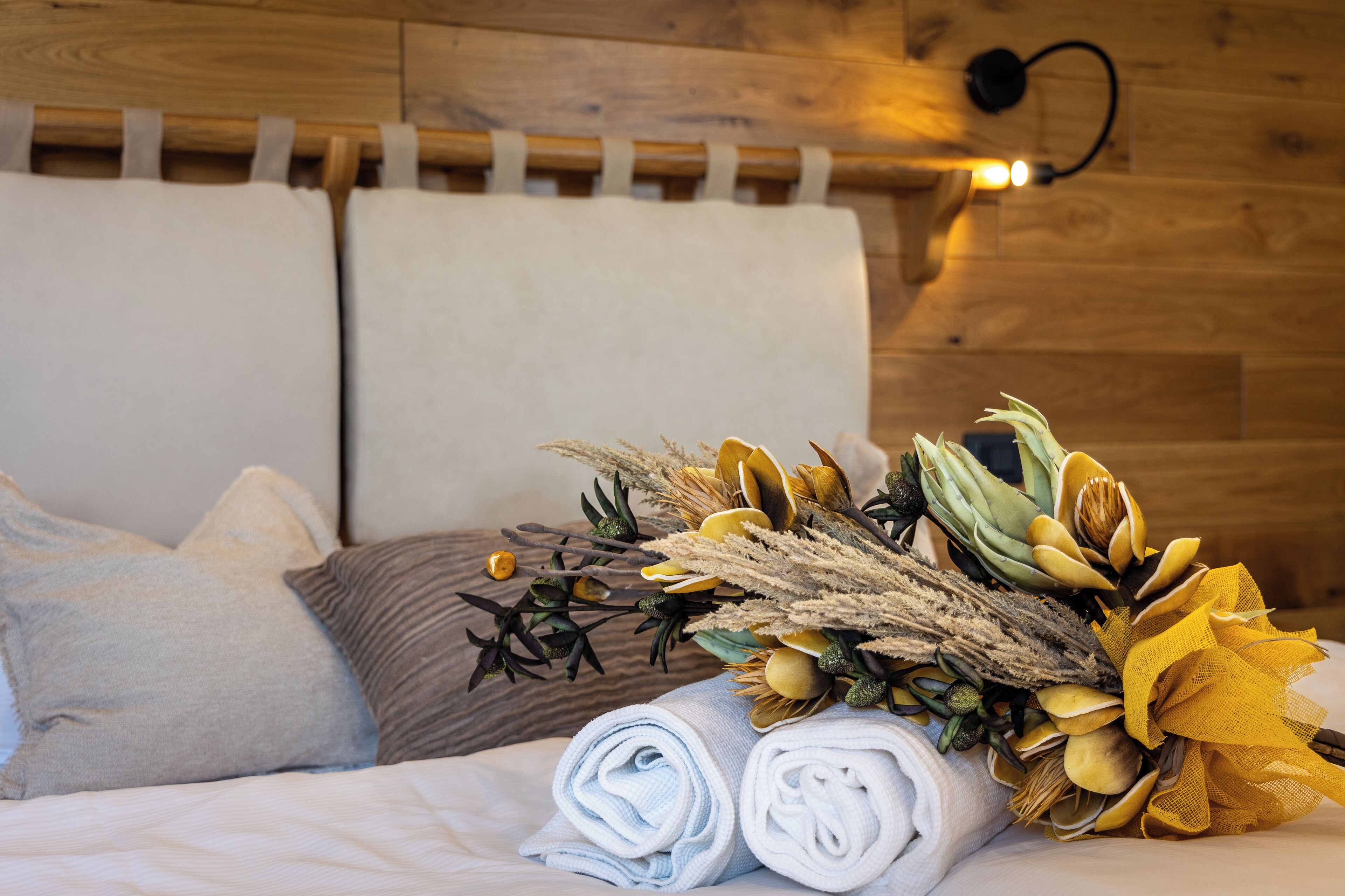 A neatly made bed with rolled towels and a decorative floral arrangement.