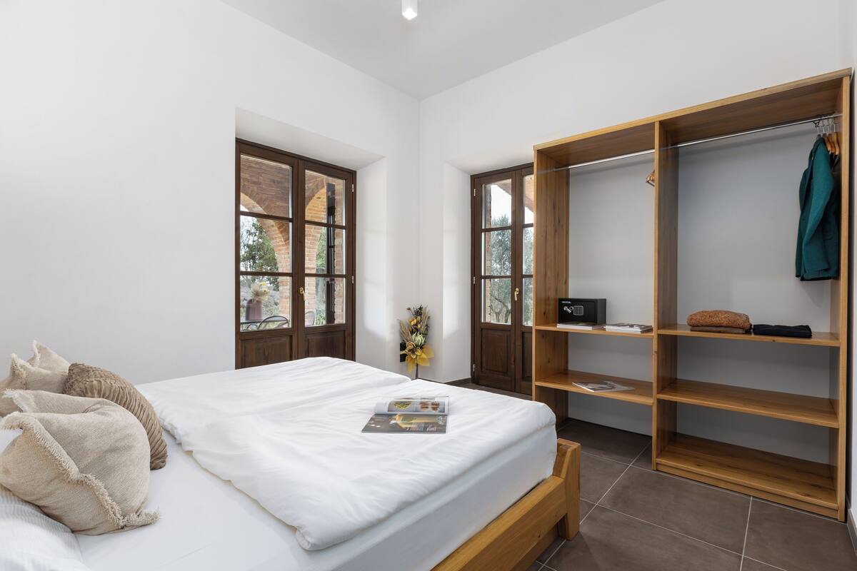 A bedroom with a bed, a wooden wardrobe, and a window with a view of trees.