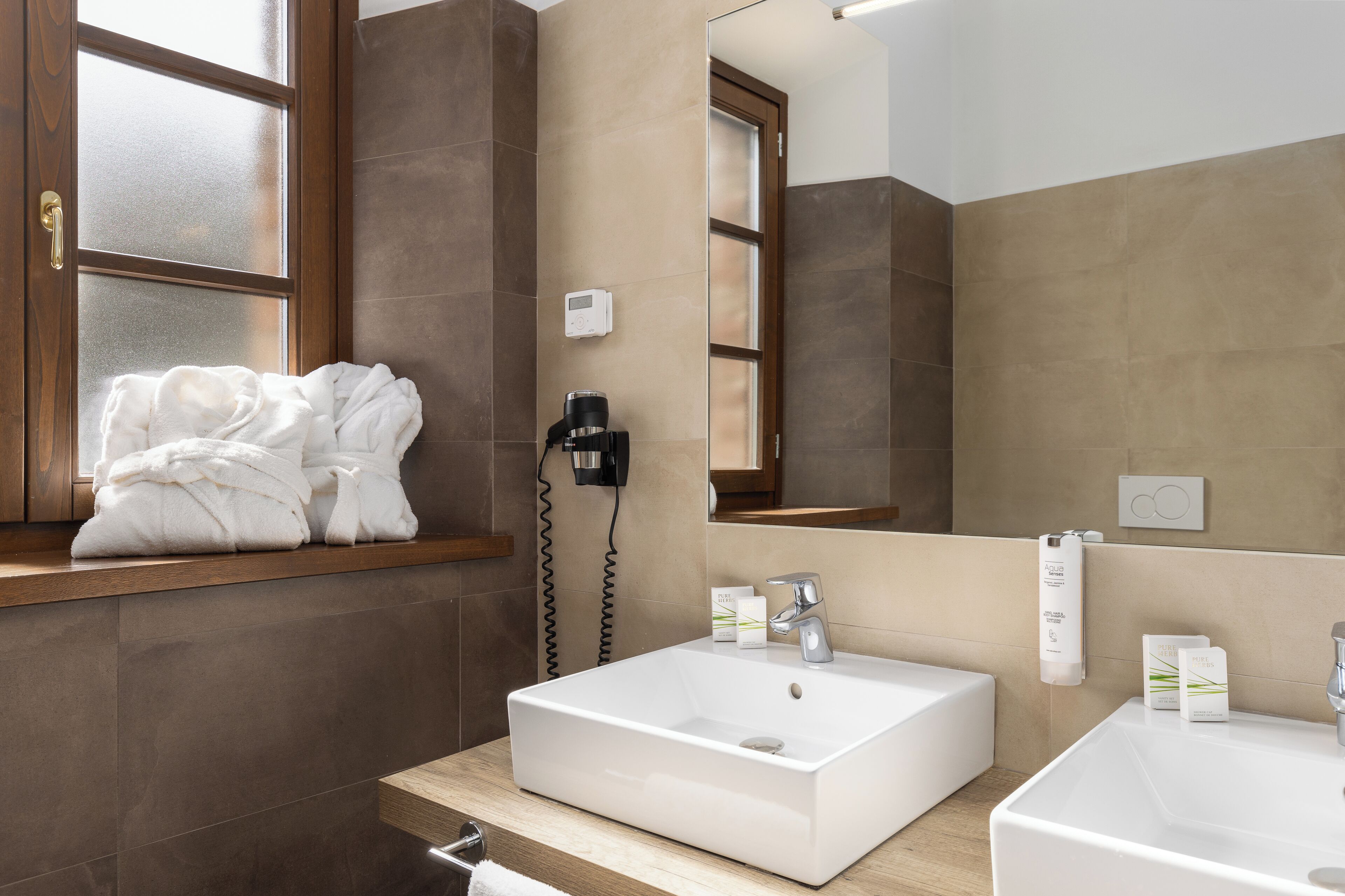 Une salle de bain moderne avec un grand miroir, deux lavabos et une fenêtre équipée d’un porte-serviettes.