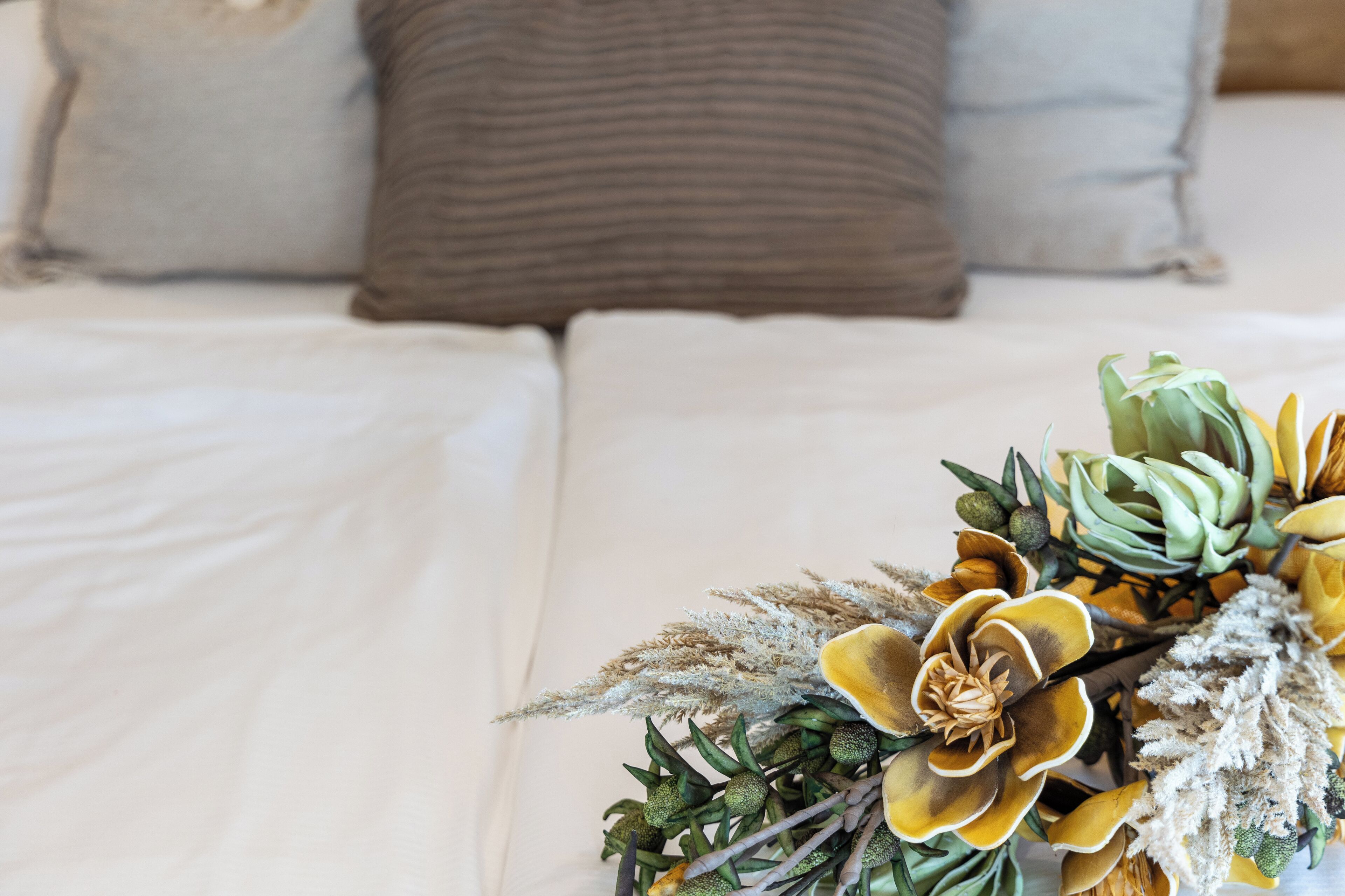Ein Bett mit weißer Bettwäsche und einer dekorativen Blumenkomposition daneben.