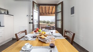 Uma sala de jantar com mesa de madeira posta para o café da manhã, incluindo frutas, pão e bebidas.